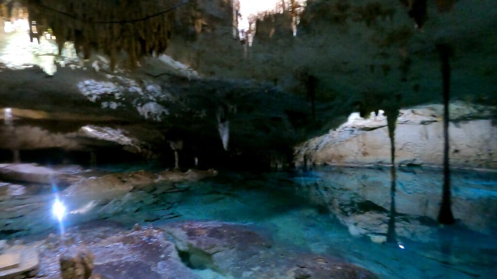 Underground cenote with crystal-clear blue water, surrounded by rock formations, captured during our family tour. 