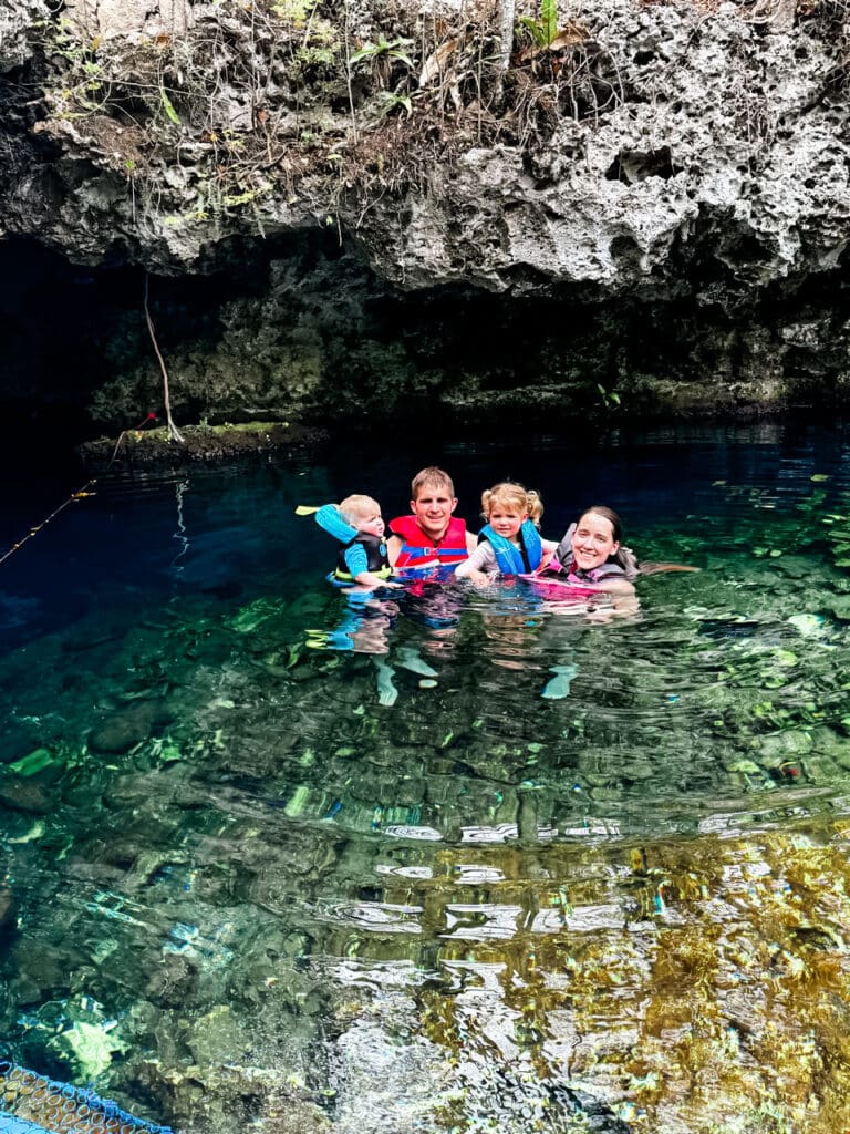 Open cenote with clear blue water surrounded by lush greenery, a highlight of our family trip near Tulum, Mexico.