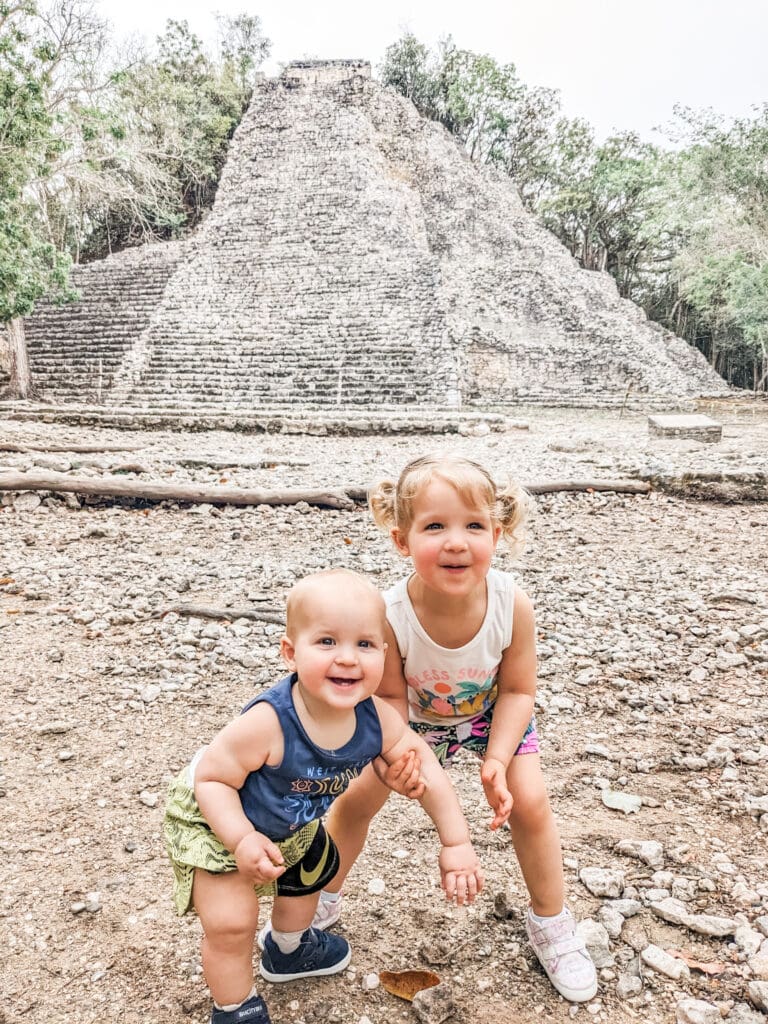 Two young children standing in front of the ancient Coba Mayan ruins, exploring the historic site during our family trip to Mexico.