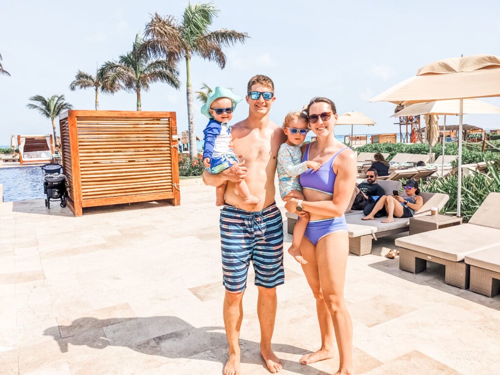 Family photo at the Hyatt Ziva Cancun, standing outside the pool with a backdrop of clear blue water and palm trees, enjoying a sunny day during our nearly free vacation using credit card points.